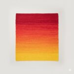 A stunning handwoven accent rug with a red, orange, and yellow sunrise ombre effect.
