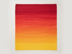 A stunning handwoven accent rug with a red, orange, and yellow sunrise ombre effect.