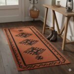 A warm, rustic hallway runner in a terracotta color with bold black traditional patterns.
