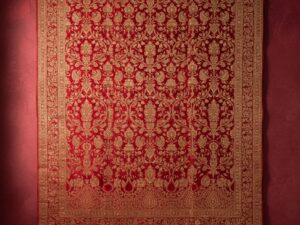A luxurious wall tapestry in brilliant red with intricate, shimmering gold patterns, inspired by a wedding sari.